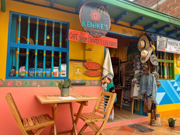 Colorful storefront in Guatapé, featuring wooden tables and vibrant decor, showcasing local crafts and traditional hats.
