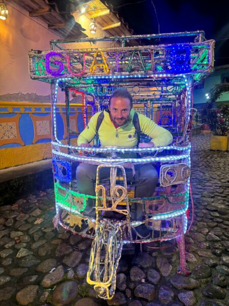 Brightly lit ochoa cart in Guatapé, Antioquia, featuring colorful decorations and cobblestone streets at night.