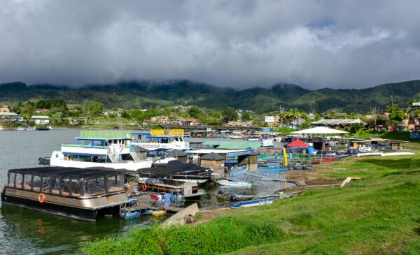Colorful boats docked along the tranquil waters of Guatapé, surrounded by lush green hills and dramatic clouds.