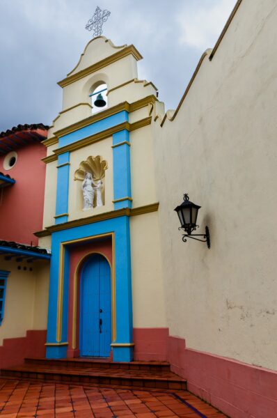 Brightly colored façade of the Capilla Hermanas de la Caridad church in Guatapé, showcasing blue doors and decorative elements.