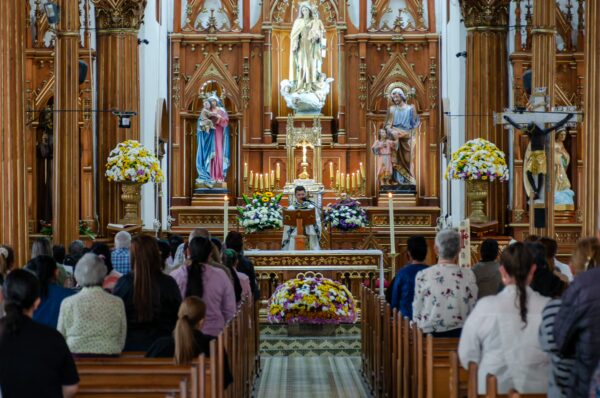 Church interior in Guatapé with a congregation seated in pews before an ornate altar and religious statues