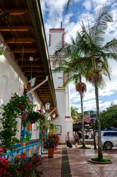 Vibrant street in Guatapé, Colombia, featuring colorful flowers, palm trees, and charming colonial architecture under a blue sky.