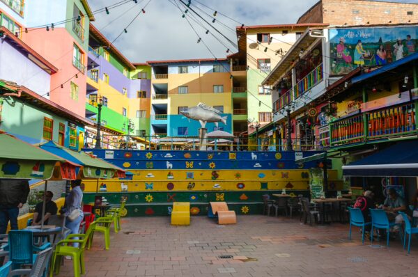 Vibrant plaza in Guatapé features colorful buildings, decorative murals, and lively seating arrangements in a bustling atmosphere.