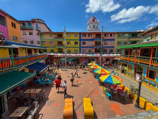 Colorful Plazoleta de Los Zócalos in Guatapé with painted buildings, café tables, and the church dome rising behind the square