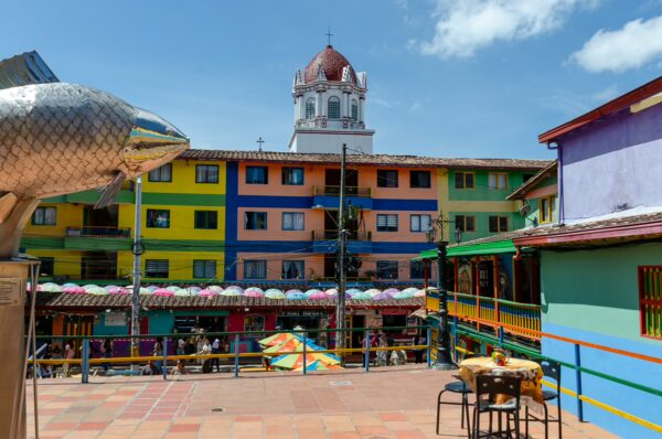 Vibrant buildings in Guatapé feature colorful facades and a lively market scene, with the distinctive tower in the background.