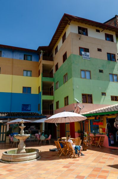 Colorful buildings surround a lively plaza in Guatapé, with a fountain and outdoor seating creating a vibrant atmosphere.