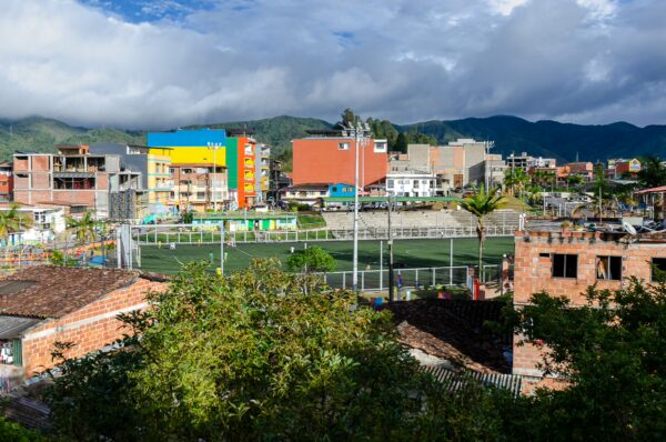 Vibrant buildings and green spaces surround a sports field in Guatapé, Colombia, with mountains in the background.