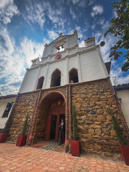 Stone-and-plaster church facade in Jordán, Chicamocha Canyon, with arched doorway and bell tower under a dramatic sky