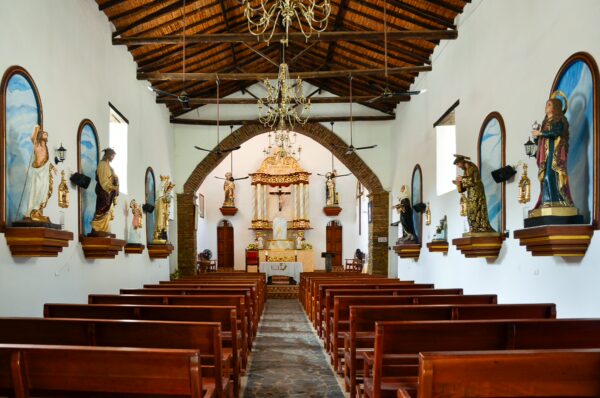 Interior of a church in Santander, Colombia, featuring wooden pews, ornate chandeliers, and religious sculptures on the walls.