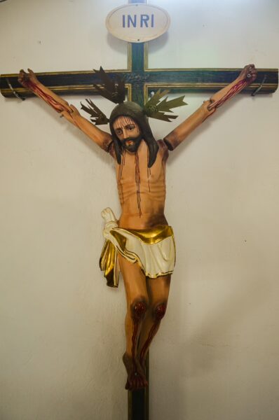 A detailed wooden crucifix with a lifelike Christ figure, displayed indoors in Santander, Colombia. The background is softly lit.