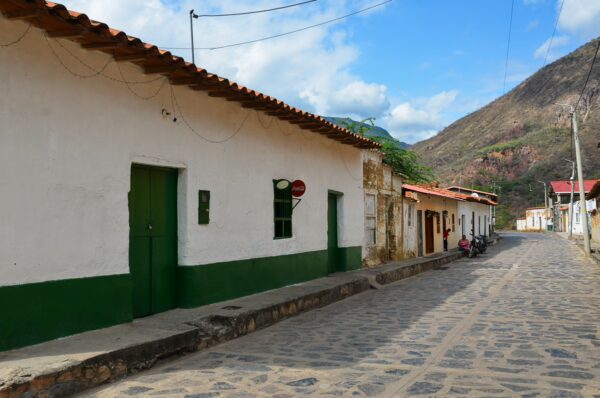 Charming street in Santander, Colombia, featuring white and green buildings, cobblestone pathway, and surrounding mountainous landscape.