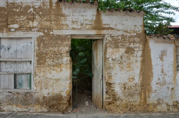 Weathered entrance of an old building in Jordan, Santander, Colombia, surrounded by lush green foliage and rustic textures.