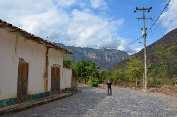 Jordan, Santander, Colombia features a cobblestone street lined with rustic houses under a blue sky, framed by mountains in the background.