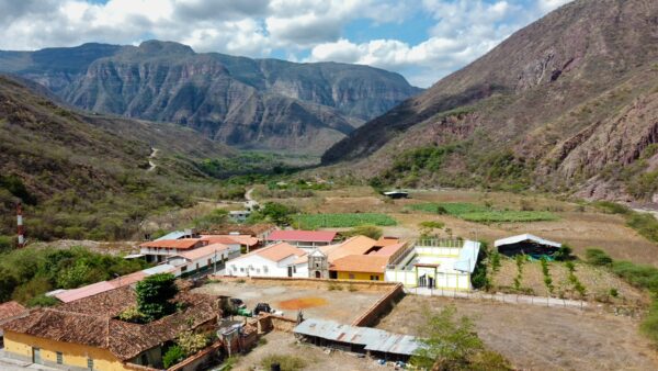 Jordan, Santander, Colombia: Scenic view of a valley with lush fields, rustic buildings, and rugged mountains under a cloudy sky.