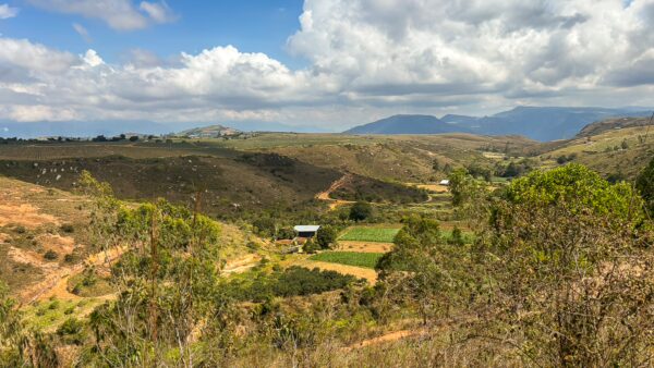 Wide view across Mesa Los Santos with rolling farmland, dirt roads, and distant mountains under a cloudy sky