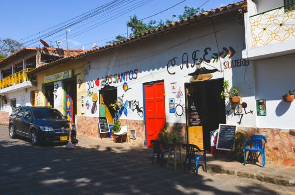 Colorful café storefront in Los Santos, Santander, with painted walls, outdoor chairs, and a parked car on a sunny street