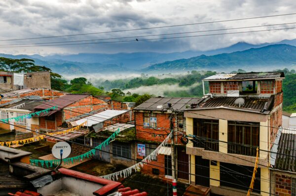 Vibrant houses with colorful fabrics overlook a misty valley in Quindío, Colombia, framed by lush green mountains.
