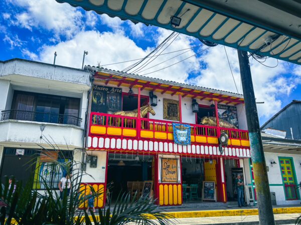 Vibrant two-story building with colorful balconies and decorative elements in Filandia, Quindio, Colombia, set against a bright blue sky.