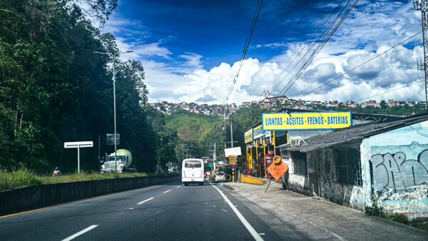 Vibrant roadside scene in Manizales, Caldas, Colombia, featuring colorful shops, green hills, and a clear blue sky.