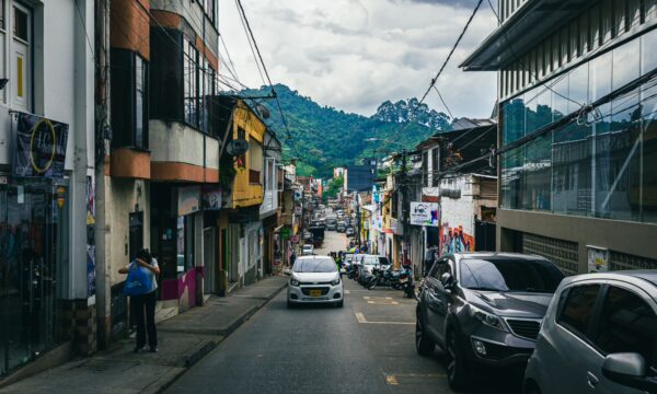 Narrow street lined with colorful buildings and parked cars, with lush green hills in the background in Santa Rosa de Cabal, Risaralda.