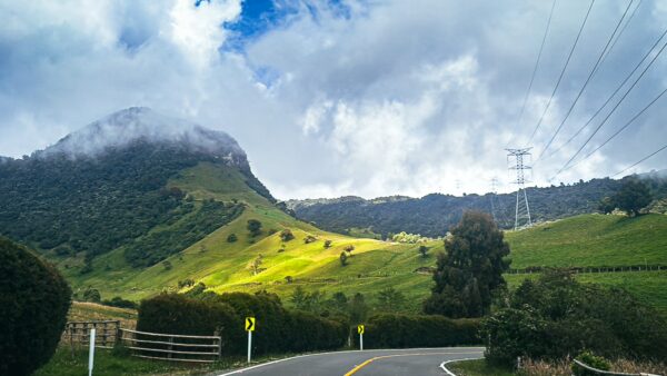 Lush green hills and cloudy skies frame the winding road near Nevado del Ruiz, Tolima, Colombia, showcasing vibrant landscapes.