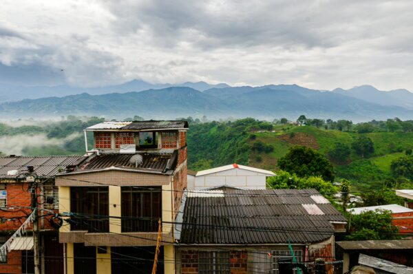 View of lush hills and misty mountains in Quindío, Colombia, with colorful buildings blending into the landscape under a cloudy sky.