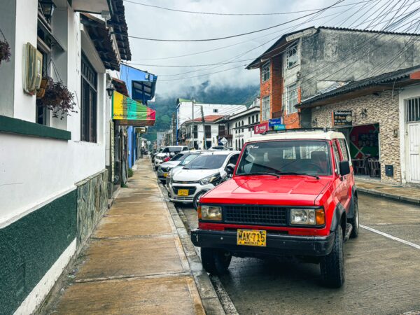 A vibrant red vehicle parked along a quiet street in Líbano, Tolima, Colombia, with quaint buildings and lush mountains in the background.