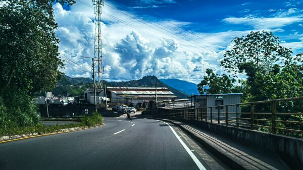 Winding road leading through lush greenery under a vibrant blue sky near Manizales, Caldas, Colombia, with distant mountains.