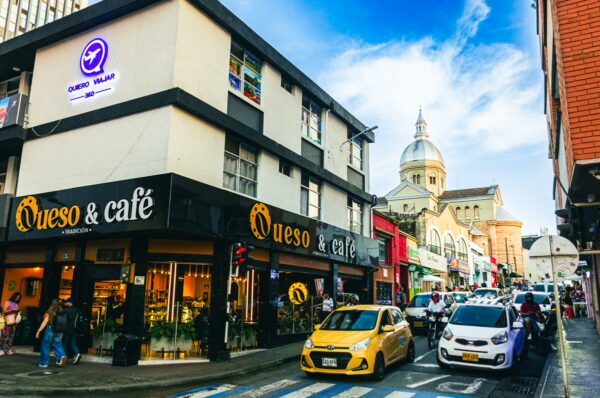 Vibrant street scene in Pereira, Risaralda, Colombia, featuring cafes, shops, and a dome building under a blue sky.