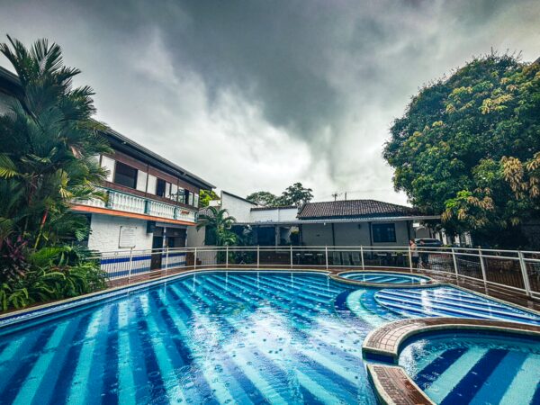 Vibrant blue-striped pool reflecting overcast skies at El Virrey Hotel Boutique, Honda, Tolima, Colombia. Lush greenery surrounds the area.