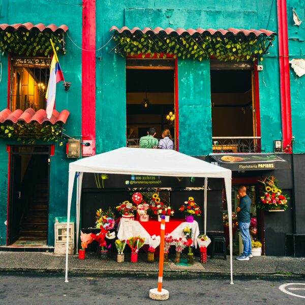 Vibrant teal building in Pereira, Colombia, features flower stalls under a white canopy and decorative plants along the facade.
