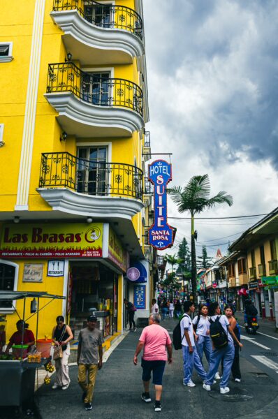 Bright yellow buildings line the street in Santa Rosa de Cabal, Colombia, with pedestrians walking past local shops and palm trees.