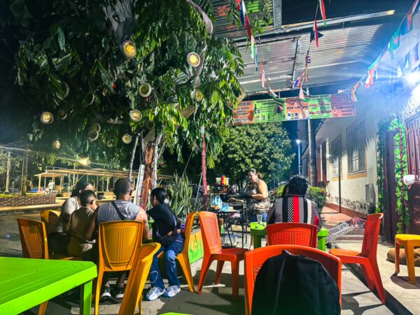 Vibrant outdoor dining scene in Villavieja, Huila, Colombia, with colorful chairs and festive decorations under a canopy of trees.