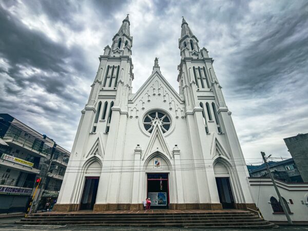 White cathedral with twin spires under a cloudy sky in Líbano, Tolima, Colombia, showcasing intricate architectural details.