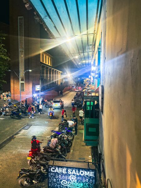 Colorful street scene in Montenegro, Quindio, Colombia, featuring packed sidewalks, parked motorcycles, and illuminated cafes.