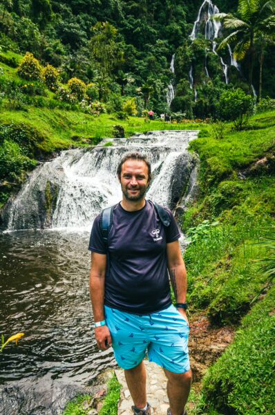 Bubbling waterfalls and lush greenery surround a traveler in shorts near Termales del Oso, Risaralda, Colombia.