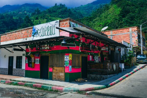 Vibrant pink and green facade of Villa Restrepo bar in Tolima, Colombia, against a backdrop of lush mountains.