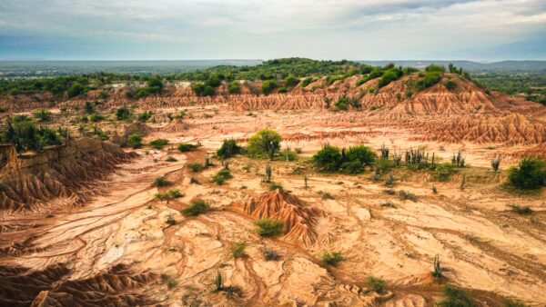 Vibrant red and orange formations stretch across the Tatacoa Desert landscape in Huila, Colombia, with scattered greenery and hills.