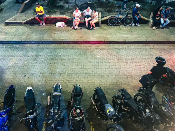 Vibrant street scene in Quindío, Colombia, featuring people relaxing on benches and parked motorcycles along the cobblestone road.