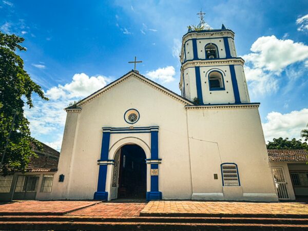 White colonial church with blue accents under a bright sky in Villavieja, Huila, Colombia, featuring a prominent bell tower.