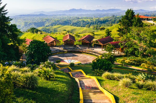 Vibrant green hills with a scenic pathway lead to rustic wooden structures at Mirador Colina Iluminada, Filandia, Quindio, Colombia.