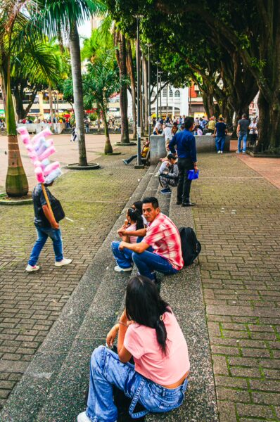 Families and locals relax on the stone benches, with palm trees lining Plaza de Bolívar in Pereira, Risaralda, Colombia.