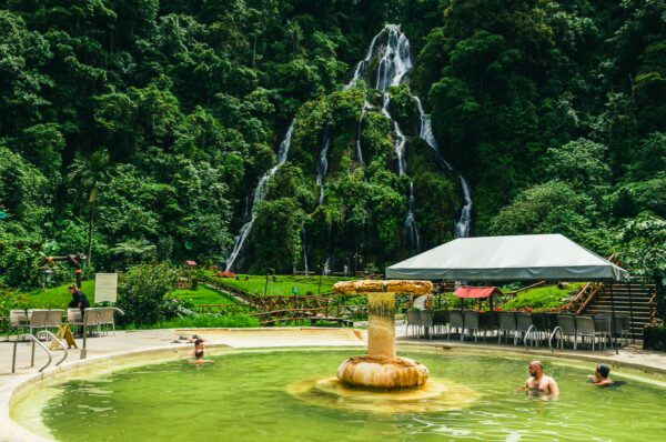 Relaxing visitors in thermal pools surrounded by lush greenery and a cascading waterfall at Termales de Rosa, Risaralda, Colombia.