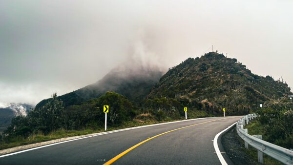 Winding road leads toward a foggy mountain at Nevado del Ruiz, showcasing lush greenery and a serene atmosphere in Tolima, Colombia.