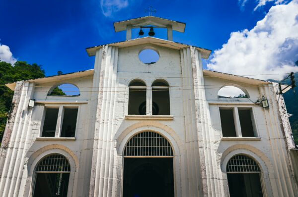 White facade of a historic building with arched windows and a bell tower against a bright blue sky in Villa Restrepo, Tolima, Colombia.