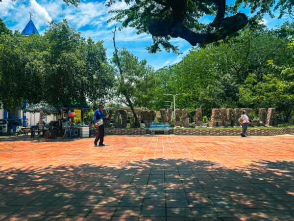 Colorful "Villavieja" sign amidst lush greenery and blue skies, with people walking on a sunlit plaza in Villavieja, Huila, Colombia.
