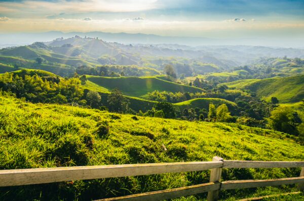 Vibrant green hills stretch across the landscape at Mirador Colina Iluminada, Filandia, Quindío, Colombia, under a soft, hazy sky.