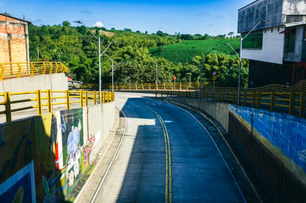 Winding road with yellow barriers, surrounded by lush green hills in Quindio, Colombia, reflecting vibrant local life.