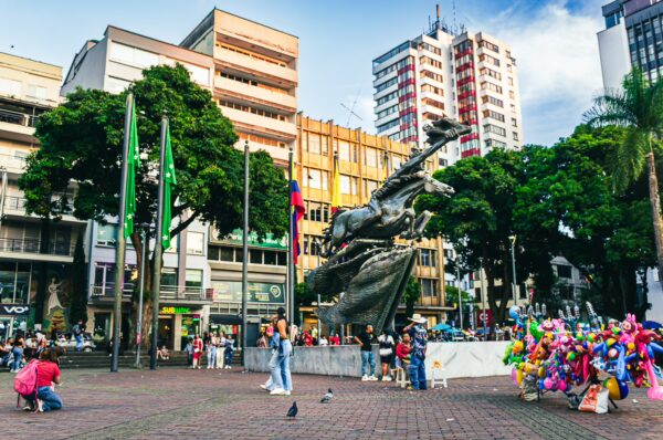 Vibrant Plaza de Bolívar in Pereira, Colombia, featuring colorful sculptures, greenery, and lively crowds enjoying the space.