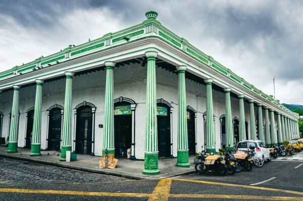 Plaza de Mercado in Honda, Tolima features green columns and a vibrant market atmosphere, showcasing local architecture and vehicles.